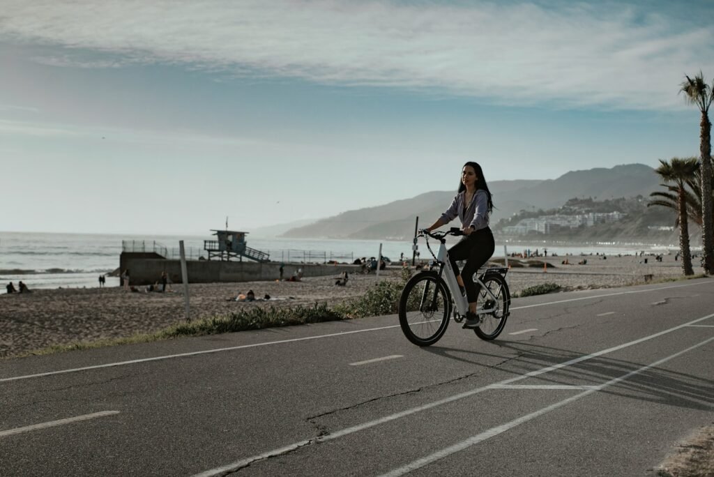 a woman riding a bike down a street next to the ocean